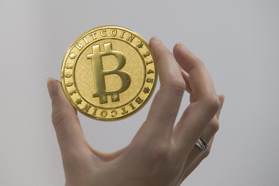 A gold metal bitcoin medallion being held between two fingers.